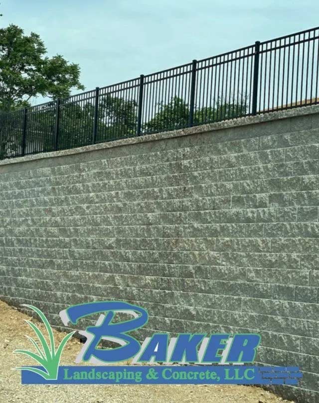 Large gray stone retaining wall topped with black metal fence