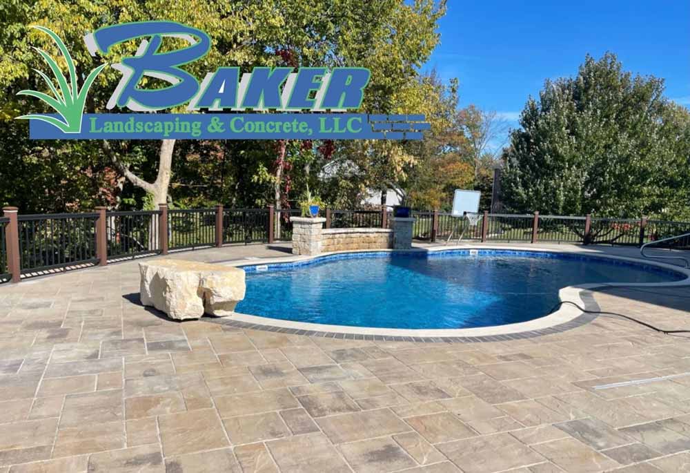 Stone patio surrounding a curved swimming pool with fence and trees