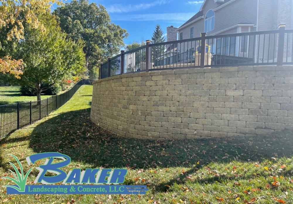 Stone retaining wall with black metal fence in landscaped yard